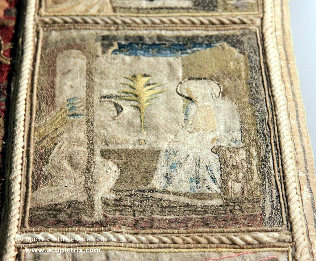 Medieval embroidery - A large red cope laying flat in a museum display case.