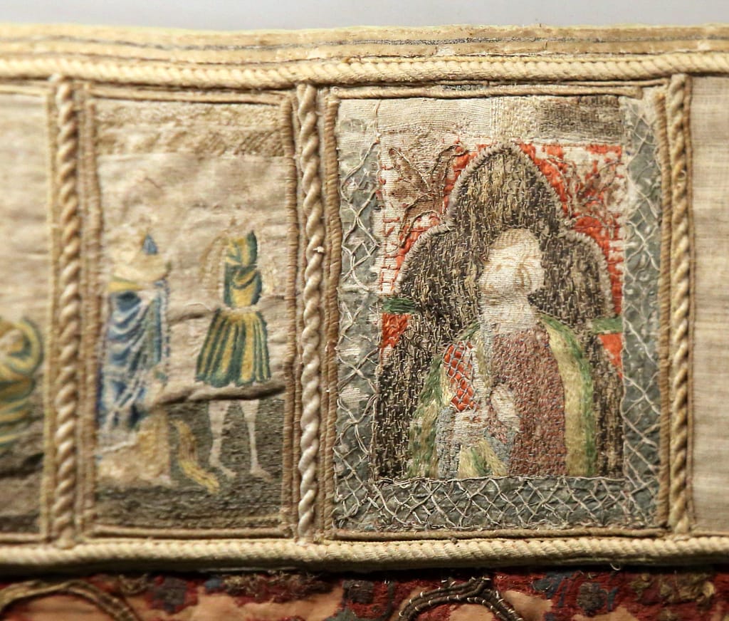 Medieval embroidery - A large red cope laying flat in a museum display case.
