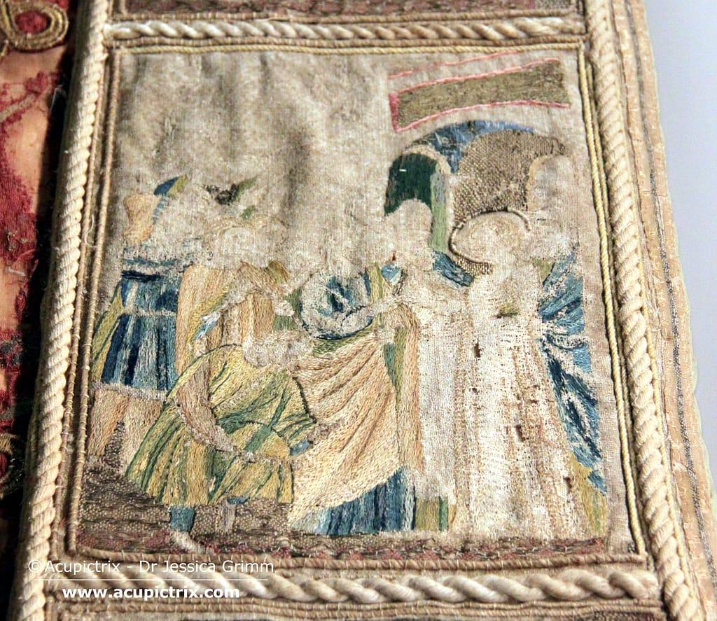 Medieval embroidery - A large red cope laying flat in a museum display case.