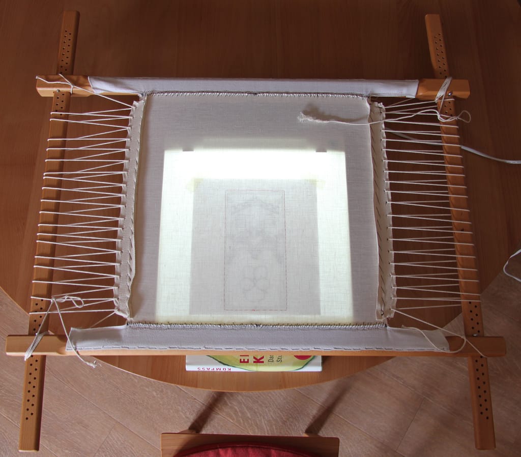 Goldwork embroidery course - a dressed slate frame propped up on a light-box on a wooden table.